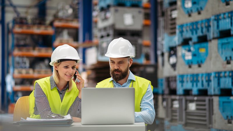 Warehouse supervisors reviewing operations on a laptop on the shop floor